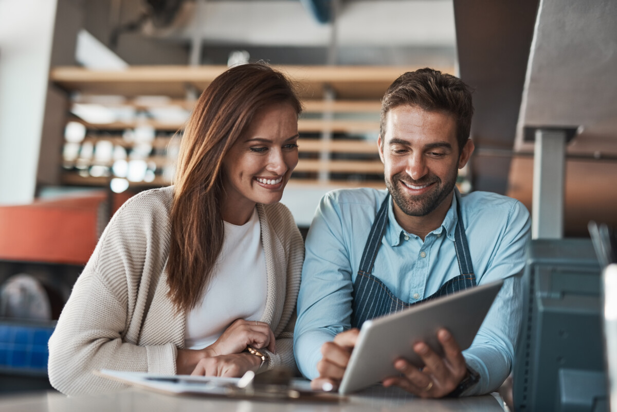 woman and man in coffee shop both looking at the same tablet