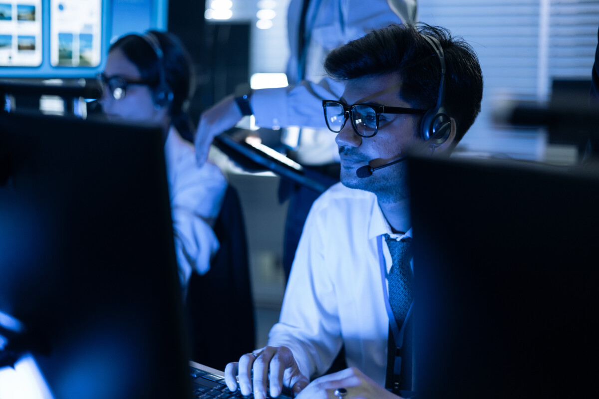 Focused male security operator with headset monitors data on screens in a high-tech control room