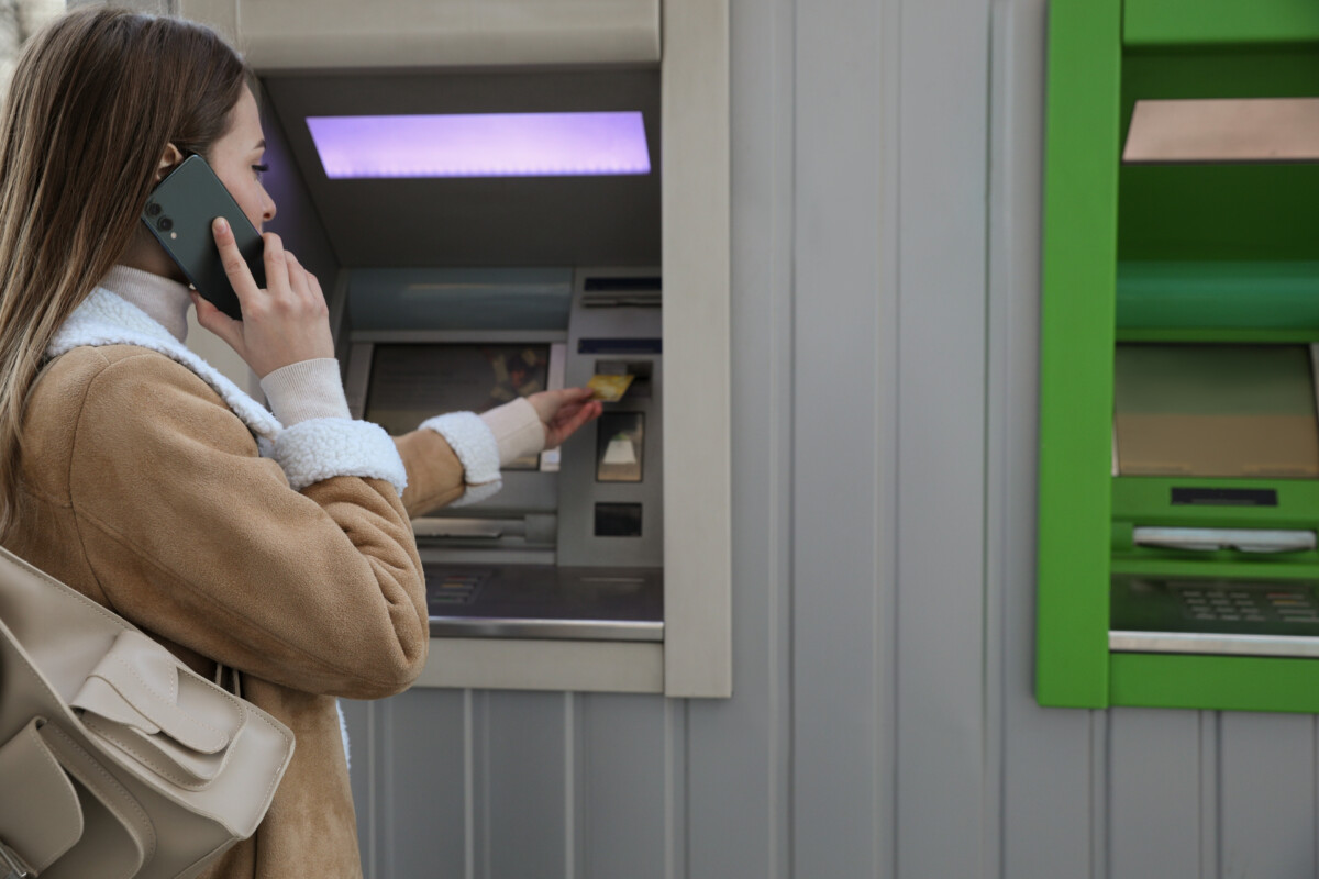 Young woman talking on a mobile phone while using cash machine