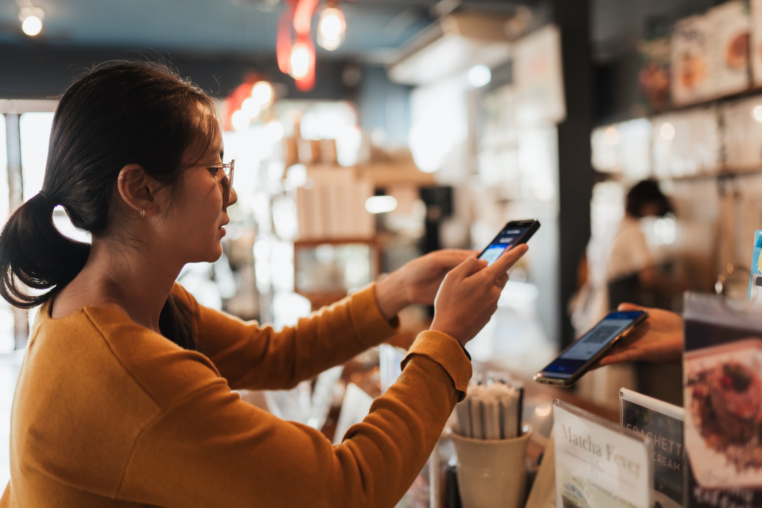 Asian woman customer scanning smartphone to pay at coffee shop counter