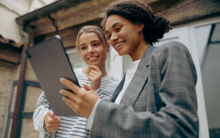 Smiling female business people standing at office terrace and using digital tablet together
