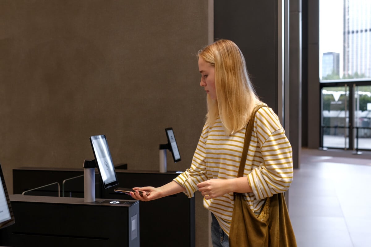 Contactless check-in with smartphone at self-service access kiosk in modern office lobby, Gen Z hybrid work and smart building security concept, copy space.