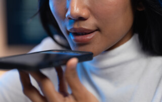 Close up of a young woman holding her smartphone near her mouth and using voice recognition or command technology